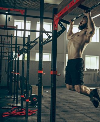 Concept: power, strength, healthy lifestyle, sport. Powerful attractive muscular man trainer do pull ups during workout at the gym